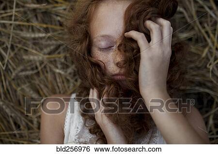 Stock Photograph - Caucasian girl laying in wheat holding hair. Fotosearch