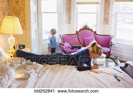 Stock Image - Caucasian girl laying on bed writing in notebook. Fotosearch