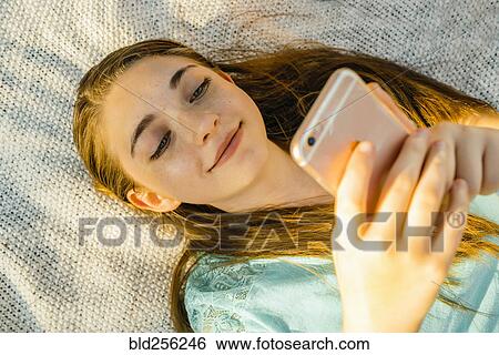 Caucasian girl laying on blanket texting on cell phone View Large Photo Image Stock Photograph - Caucasian girl laying on blanket texting on cell phone. Fotosearch