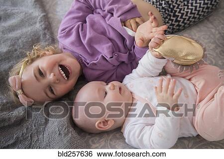 Stock Photograph - Caucasian girl laying on floor with baby sister. Fotosearch