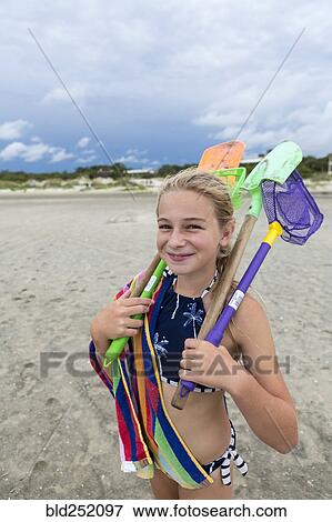 Stock Photo - Caucasian girl on beach carrying net and shovels. Fotosearch