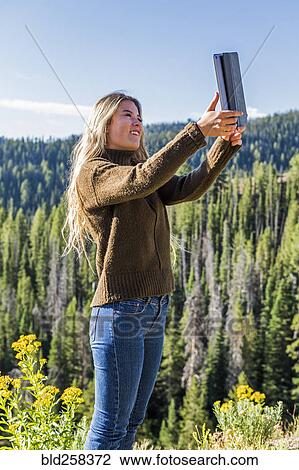 Stock Image - Caucasian girl photographing landscape with digital tablet. Fotosearch