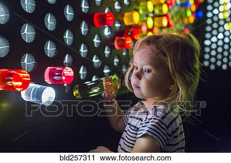 Stock Image - Caucasian girl placing colorful game pieces on puzzle wall. Fotosearch