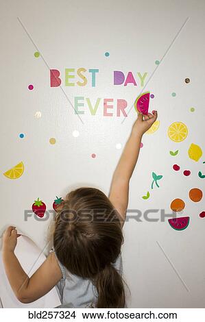 Picture - Caucasian girl placing watermelon decoration on wall. Fotosearch