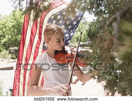 Stock Image - Caucasian girl playing violin near American flag. Fotosearch