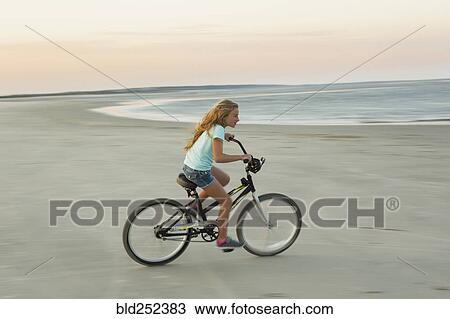 Stock Image - Caucasian girl riding bicycle on beach. Fotosearch