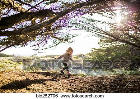 Stock Photograph - Caucasian girl running under tree branches. Fotosearch