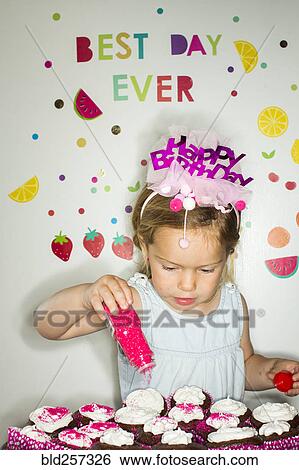 Stock Photograph - Caucasian girl s1inkling s1inkles on tray of cupcakes for birthday. Fotosearch