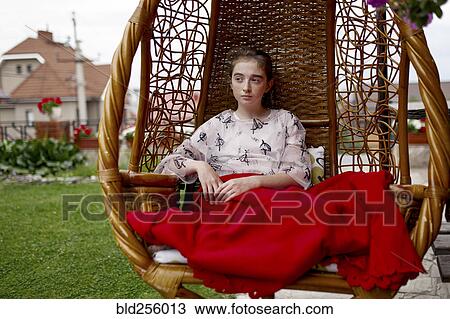 Stock Image - Caucasian girl sitting in hanging chair outdoors. Fotosearch