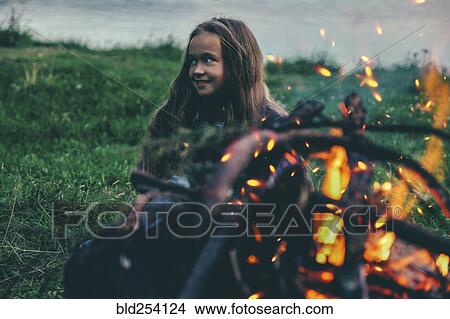 Picture - Caucasian girl sitting near campfire. Fotosearch