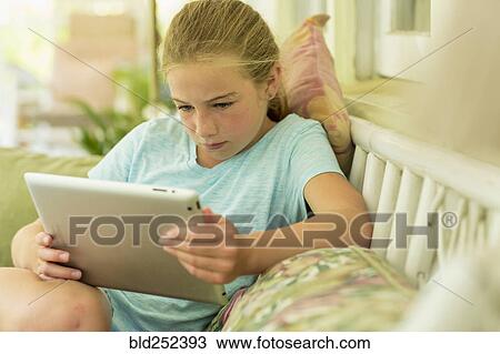 Stock Image - Caucasian girl sitting on sofa watching digital tablet. Fotosearch