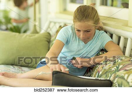 Stock Photo - Caucasian girl sitting on sofa watching digital tablet. Fotosearch
