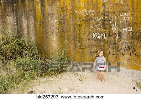 Stock Image - Caucasian girl standing in sand near graffiti wall. Fotosearch