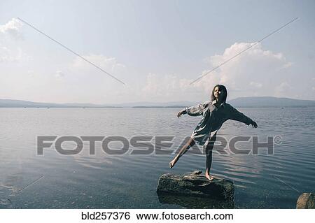 Stock Photograph - Caucasian girl standing on rock in lake. Fotosearch