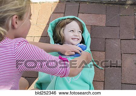 Stock Photograph - Caucasian girl talking brother into sweatshirt. Fotosearch
