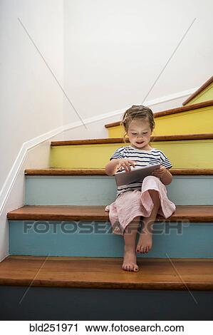 Stock Image - Caucasian girl using digital tablet on staircase. Fotosearch