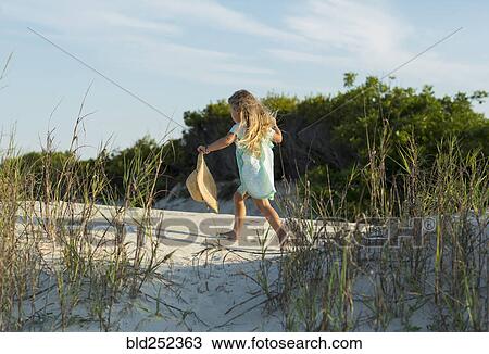 Stock Image - Caucasian girl walking on beach holding hat. Fotosearch