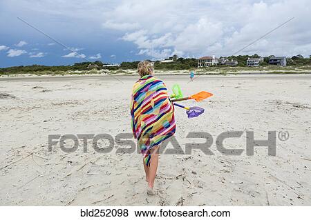 Stock Photo - Caucasian girl walking on beach carrying net and shovels. Fotosearch