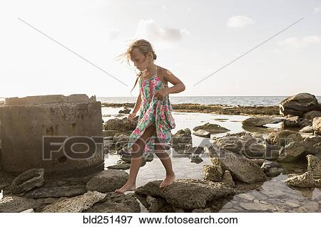Stock Photo - Caucasian girl walking on rocks at beach. Fotosearch