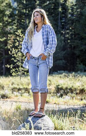 Stock Image - Caucasian girl wearing plaid shirt standing on rock. Fotosearch