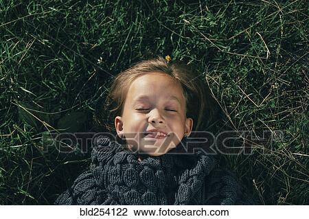 Stock Image - Caucasian girl wearing sweater laying in grass. Fotosearch
