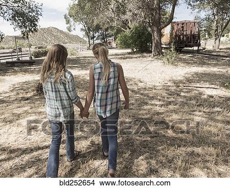Caucasian girls holding hands walking in field View Large Photo Image Picture - Caucasian girls holding hands walking in field. Fotosearch