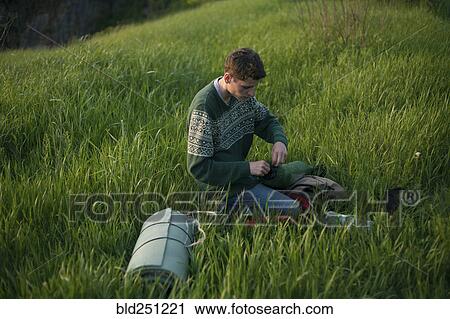 Stock Image - Caucasian hiker kneeling in grass. Fotosearch