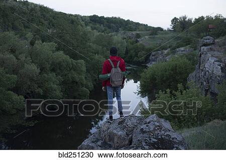 Stock Image - Caucasian hiker standing on rock near river. Fotosearch