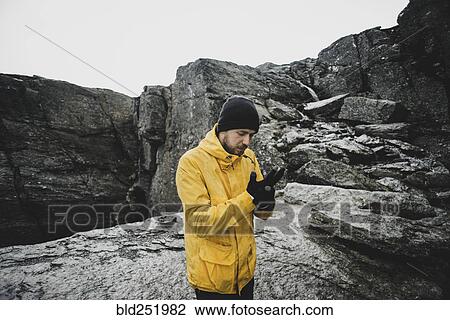 Stock Image - Caucasian man adjusting gloves on mountain. Fotosearch
