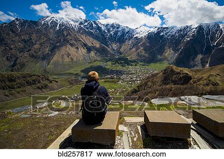 Stock Photo - Caucasian man admiring scenic view of village in valley. Fotosearch