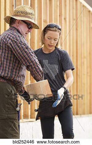 Stock Photograph - Caucasian man and woman carrying lumber at construction site. Fotosearch