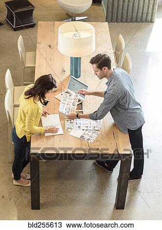Stock Image - Caucasian man and woman examining photographs at table. Fotosearch