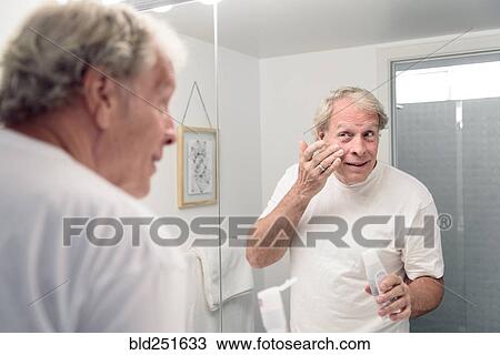 Caucasian man applying lotion to face in mirror View Large Photo Image Stock Image - Caucasian man applying lotion to face in mirror. Fotosearch