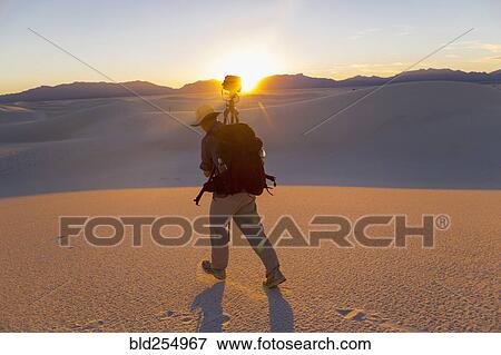 Stock Photo - Caucasian man carrying camera and tripod in desert. Fotosearch