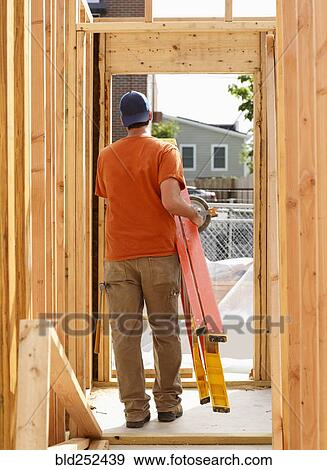 Stock Photo - Caucasian man carrying ladder at construction site. Fotosearch