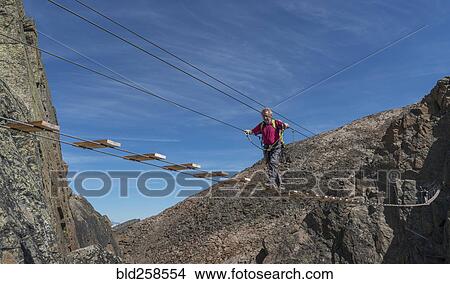 Picture - Caucasian man crossing rope bridge on mountain. Fotosearch