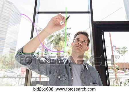 Stock Photo - Caucasian man drawing diagram on glass wall. Fotosearch