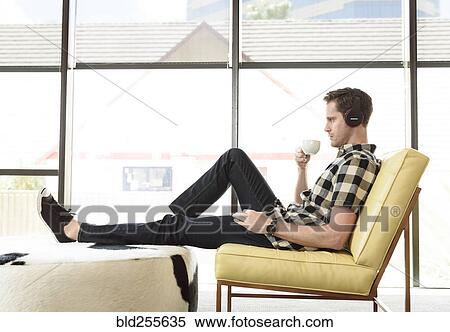 Stock Photography - Caucasian man drinking coffee and listening to headphones. Fotosearch