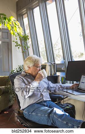 Picture - Caucasian man drinking coffee and using laptop. Fotosearch