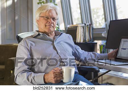 Stock Image - Caucasian man drinking coffee and using laptop. Fotosearch