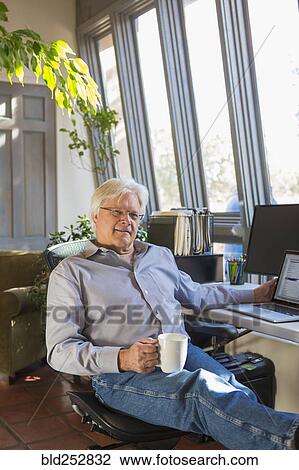 Stock Image - Caucasian man drinking coffee and using laptop. Fotosearch