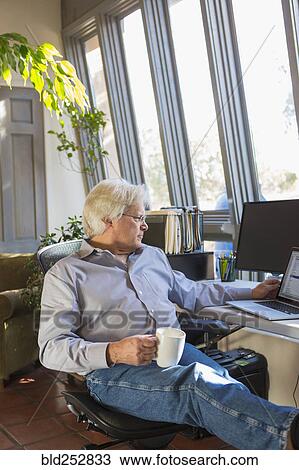 Stock Image - Caucasian man drinking coffee and using laptop. Fotosearch