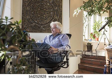 Stock Photo - Caucasian man drinking coffee with feet up on desk. Fotosearch