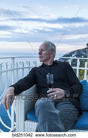 Stock Image - Caucasian man drinking wine on waterfront balcony. Fotosearch