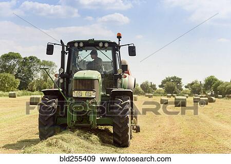 Stock Photo - Caucasian man driving tractor baling hay. Fotosearch