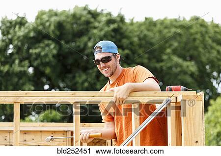 Stock Image - Caucasian man hammering at construction site. Fotosearch