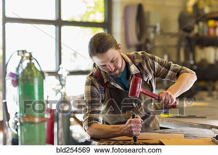 Stock Photo - Caucasian man hammering leather in a workshop. Fotosearch