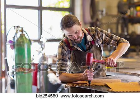 Stock Image - Caucasian man hammering leather. Fotosearch