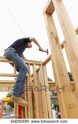 Stock Image - Caucasian man hammering nail at construction site. Fotosearch