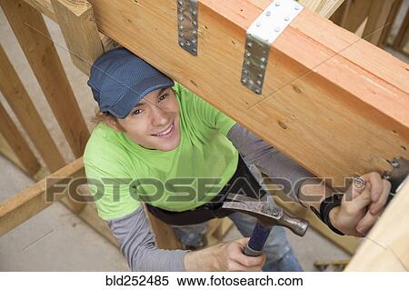 Stock Photography - Caucasian man hammering nail at construction site. Fotosearch